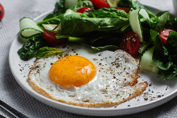 istock Fried egg with spinach, tomato and cucumber salad in a white plate. Healthy breakfast 2215696703