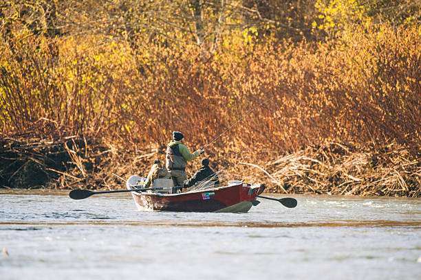 Young couple drifting down river in rowboat fishing for salmon and steelhead trout, autumn, distant view. Guided drift fishing trip, Washington State