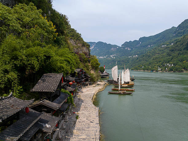 This photo captures the charming riverside village at the Three Gorges Family scenic area, showcasing traditional architecture nestled along the Yangtze River with boats gently floating by.