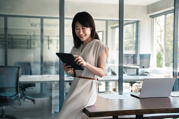 istock Asian middle-aged woman using tablet reading news browsing, doing online work, business learning or communication. Smiling ceo entrepreneur businesswoman leader using touchsceen pc device in office 2215714057