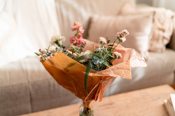 Elegant flower bouquet in warm wrapping, illuminated by soft natural light indoors on a rustic table.