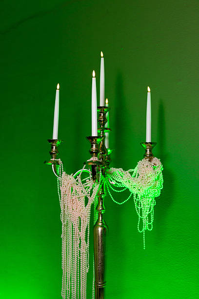 Elegant candelabra adorned with draped pearl necklaces and glowing candles, set against a vivid green-lit background for festive decor.