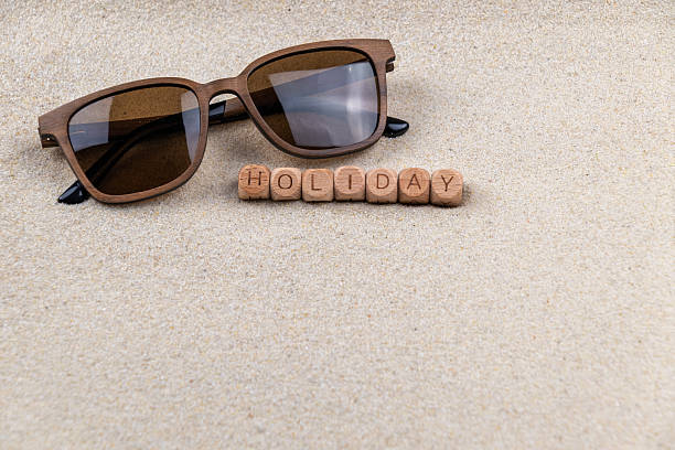 Sunglasses on sandy beach with Wooden blocks spelling holiday. copy space