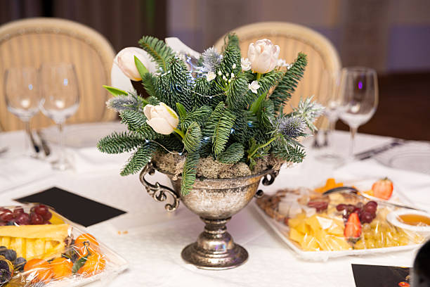 Festive winter table arrangement with soft pink tulips, pine branches, and fairy lights in a vintage silver vase for holiday decor.