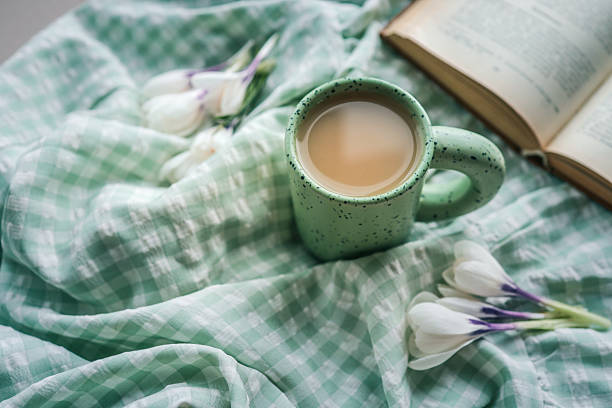 istock Green speckled ceramic mug with coffee placed on soft green checkered fabric alongside white crocus flowers and an open book, creating a peaceful springtime scene 2215729831
