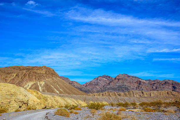 Looking across the entrance to Hole in the Wall Canyon, layers of golden sedimentary rock rise against the rugged peaks beyond. Shaped by ancient seas, earthquakes, and floods, this wild landscape reveals the raw geological history that makes Death Valley so extraordinary.  Hole in the Wall Canyon is in Death Valley National Park near Furnace Creek, California, USA.