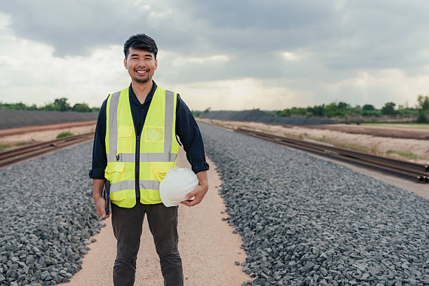 istock Smiling civil engineer standing on railway construction site, holding helmet and tablet confidently. 2215732854