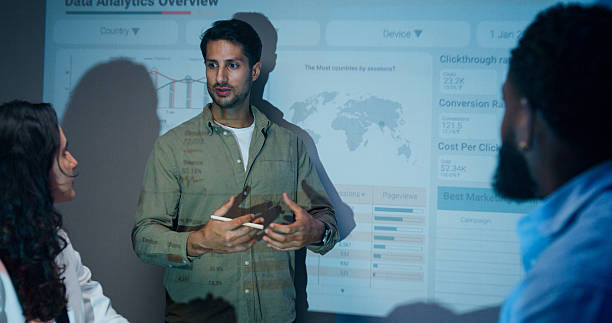 istock Group of businesspeople working late analyzing financial data displayed on projection screen while discussing strategy and planning for future business growth at office night. Finance meeting. 2215733604