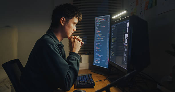 istock Young man software engineer experience emotional stress while working late on AI prompt coding on computer in bedroom at home night. Software developer, artificial intelligence and programmer. 2215733977