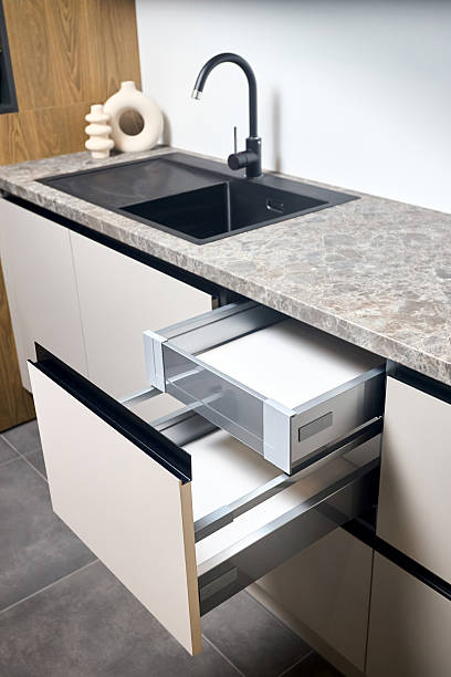istock Horizontal sliding pull out drawer cabinet shelves storage in kitchen cupboard with beige panels under stoneware countertop toptable black sink basin and facet. 2215736450