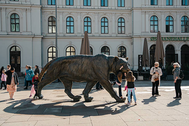 Oslo, Norway - Apr 13, 2024: People and children interact with the famous bronze tiger statue near Oslo Central Station on a sunny day in Norway.