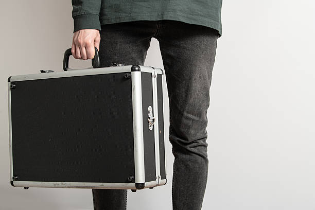 istock Individual stands confidently while grasping a black briefcase, showcasing a modern indoor environment. The attire is casual yet stylish, highlighting a sense of purpose 2215740087
