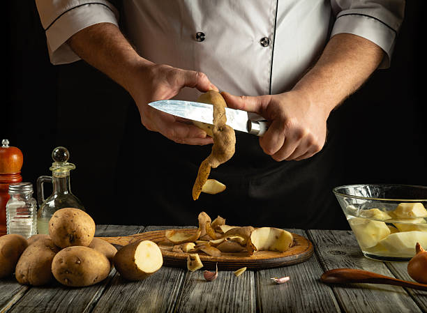 A chef skillfully peels fresh potatoes in a rustic kitchen setting. The soft glow of dusk illuminates the scene, highlighting the chef's focused work and the raw ingredients around