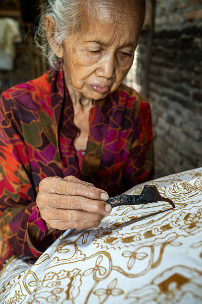 istock Indonesian woman making batik with canting tool and hot wax 2215755449