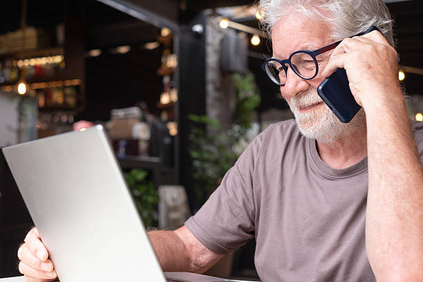 istock A smiling bearded senior man sits in a cafe using his laptop and smartphone. An elderly business man uses technology expressing confidence and contentment in a relaxed atmosphere. 2215756305