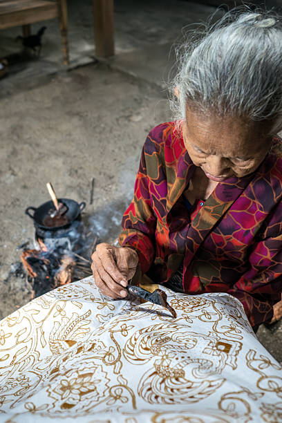 Indonesian woman making batik with canting and hot wax over fire