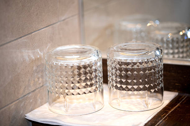 Two clean glass tumblers placed upside down on a white napkin in a modern hotel bathroom. A minimalist and hygienic composition perfect for hospitality visuals, personal hygiene themes, hotel amenities, and interior design content.