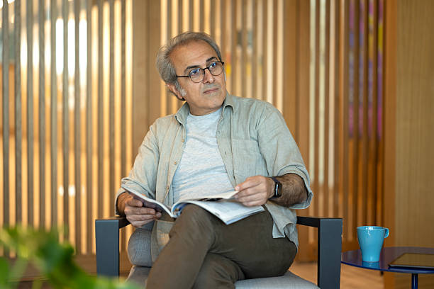 istock Senior Man Relaxing On Sofa At Home Reading Magazine 2215760131