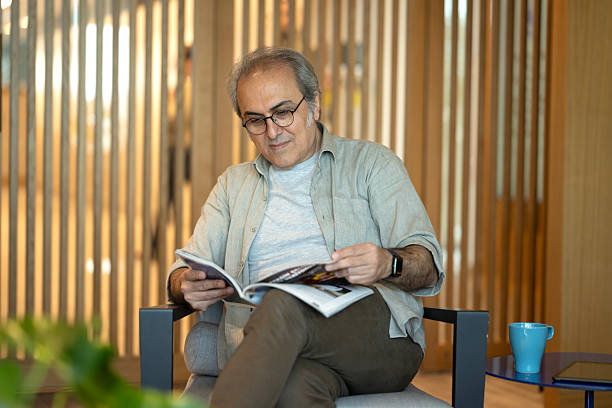 istock Senior Man Relaxing On Sofa At Home Reading Magazine 2215760132