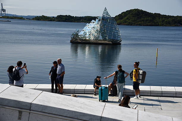 She Lies in Oslo located at the Fjord next to the Opera House is a public sculpture by Monica Bonvicini made of stainless steel and glass panels. Captured during summer season with some tourists on the rooftop of the Opera house.