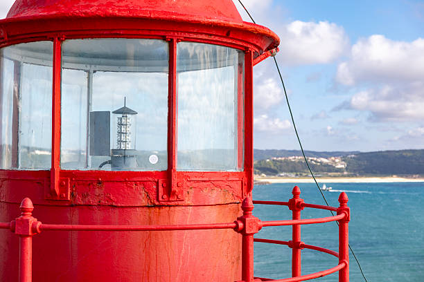 Close-up photo of the iconic red lighthouse in Nazaré, overlooking surfers on giant waves, Portugal