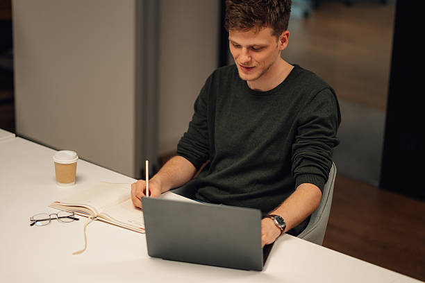 istock Young man working on laptop and taking notes in office 2215785883