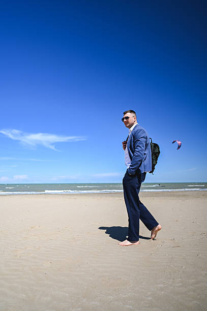 Businessman walking barefoot on a sandy beach enjoying summer vacation