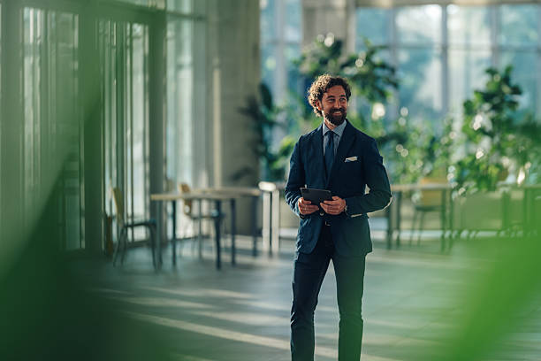 Smiling businessman holding digital tablet walking in modern office