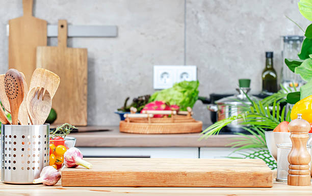 istock Kitchen table with cutting board, spice grinder and utensils, countertop with pans on induction hob, knives 2215791796