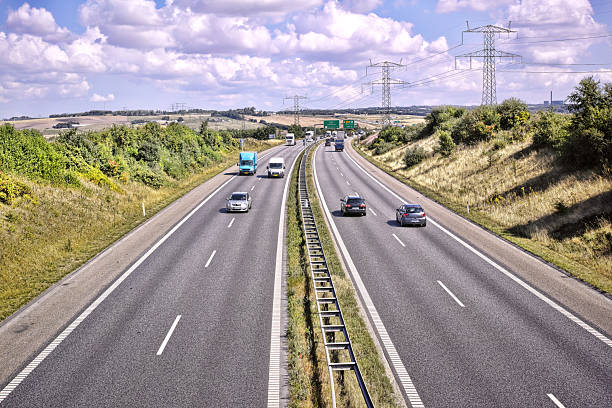 A picturesque highway stretches through verdant hills adorned with lush greenery. Cars traverse smoothly while fluffy clouds float above, creating a tranquil and peaceful scene that reflects modern connectivity and natural charm.
