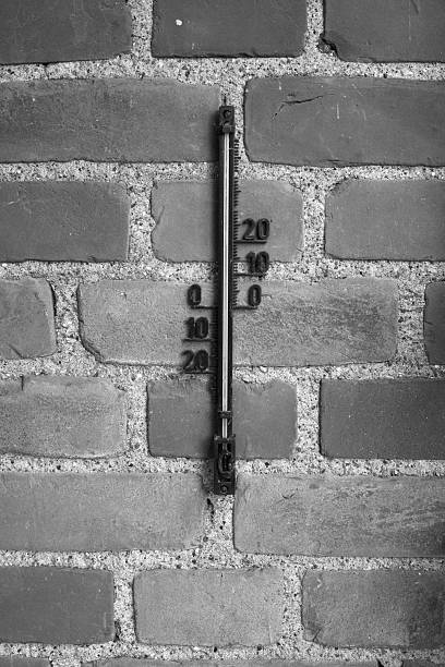A classic analog thermometer mounted on a rustic brick wall, displayed in a striking black-and-white composition. Emphasizes the contrast of textures and tones, delivering an aesthetic nostalgic atmosphere.