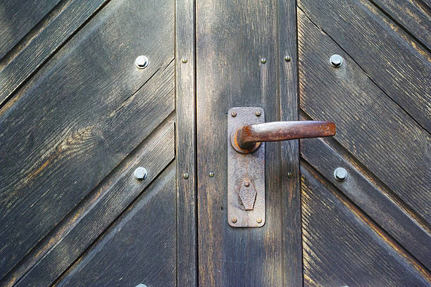 A close-up view of a weathered wooden door with a rustic iron handle. The craftsmanship and aged patina evoke a timeless charm, showcasing the marriage of utility and aesthetic appeal in vintage design.