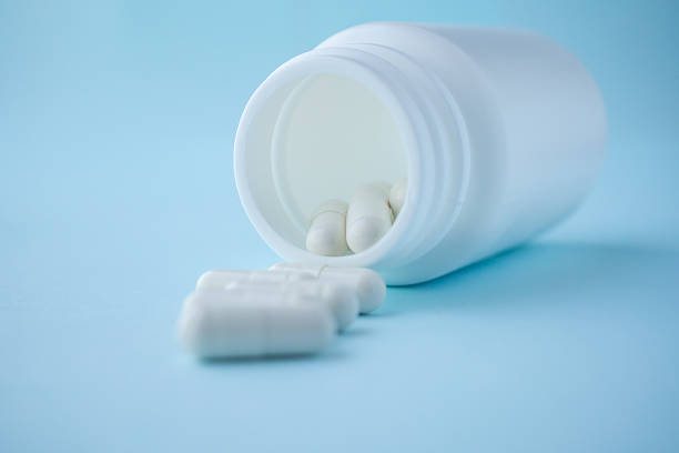 istock medicine pills capsule spilling out of bottle on blue background 2215802400