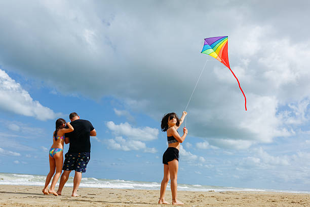 istock rear view of a dad and two daughters standing on the beach flying a kite 2215812006