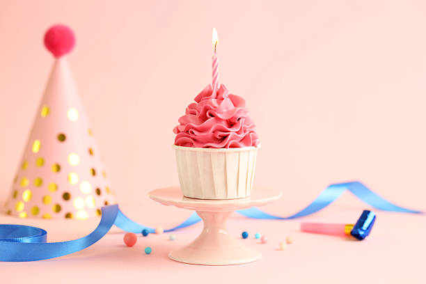 istock Tasty cupcake with burning candle and party cone on pink background 2215824911