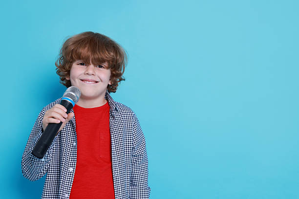 istock Little boy with microphone pretending to be singer on light blue background, space for text. Dreaming about future profession 2215825041