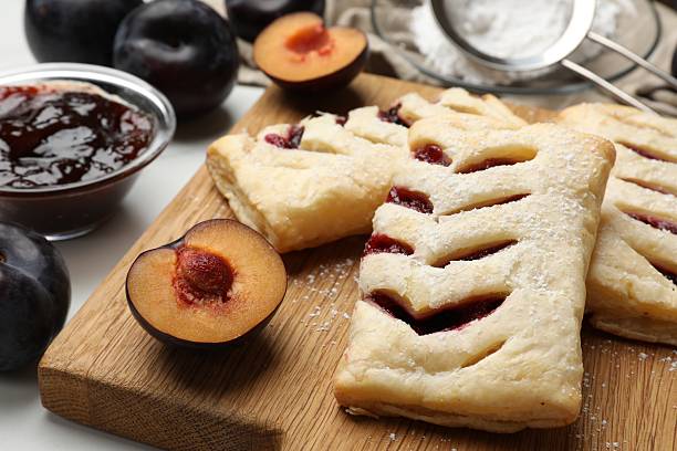 istock Delicious puff pastries and plums on white wooden table, closeup 2215829563
