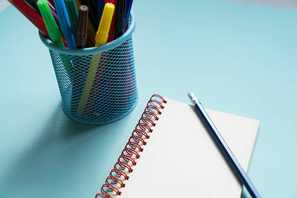 Colored pencils in a pencil case on a blue background with a note pad