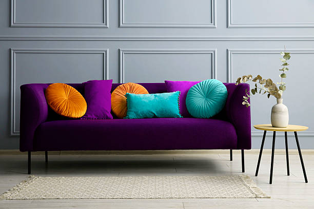 istock Stylish purple sofa with cushions and table near grey wall 2215831024