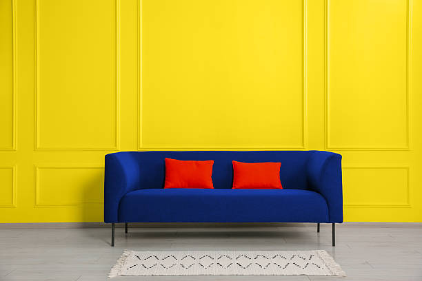 istock Stylish blue sofa with red cushions near yellow wall 2215831026