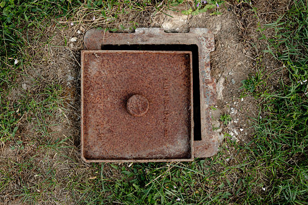 istock Old Rusty Metal Cover Embedded in Overgrown Grass On Ground Surface 2215833175