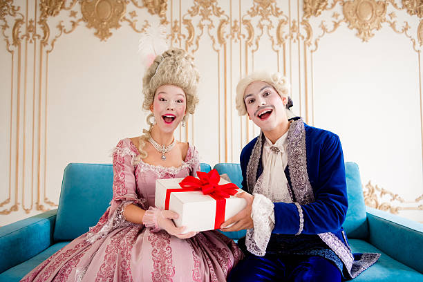 istock Cheerful couple dressed in elegant historical costumes presenting a gift in a luxurious baroque-styled palace interior. 2215833634