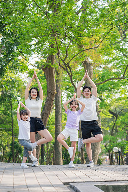 istock Family Practicing Yoga Outdoors in a Park Settings Under Trees 2215836323