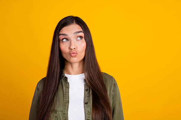istock Young woman with long hair making a playful face expression against a vibrant yellow backdrop 2215836574