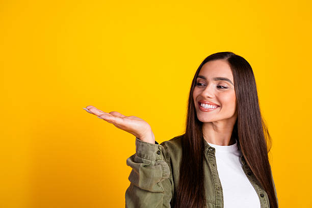 istock Charming young woman in a casual outfit gesturing and smiling cheerfully against a vibrant yellow background 2215836623