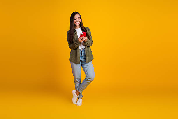 istock Young woman standing against a vibrant yellow background using a smartphone in a casual stylish outfit, looking happy 2215836689