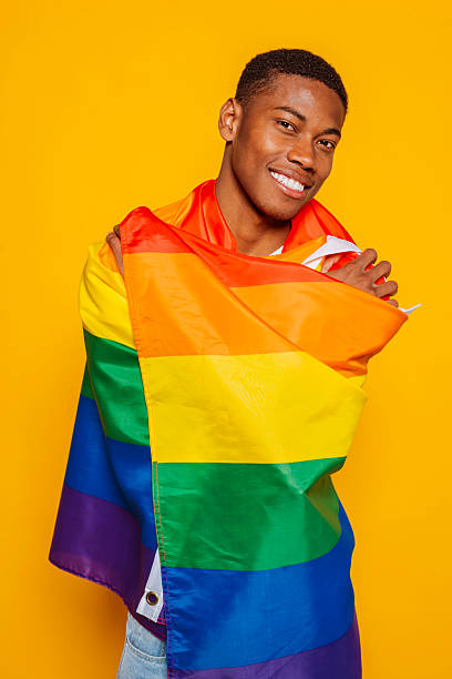 istock Young man embracing rainbow flag, smiling on yellow background: lgbtq+ pride and inclusivity 2215837384