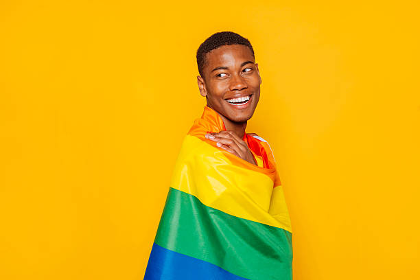 istock Happy black man smiling and holding rainbow flag on yellow background 2215837444