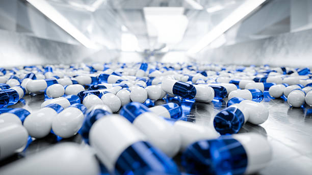 Blue and white capsules scattered on a shiny metallic surface Blue and white capsules scattered on a shiny metallic surface in a pharmaceutical production setting. CGI render sorter machine stock pictures, royalty-free photos & images