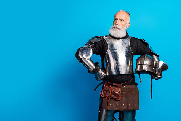 istock Elderly bearded man wearing medieval-style metal armor posing against a blue background, representing historical themes and noble traits 2215837622